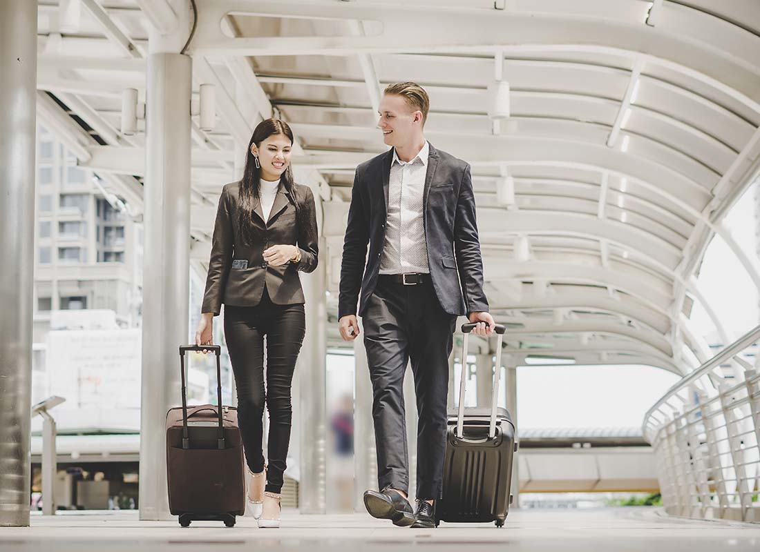 International Commercial Insurance - Business Man and Woman Going on an International Business Trip Walking Away From the Camera and Pulling Luggage in an Airport Terminal